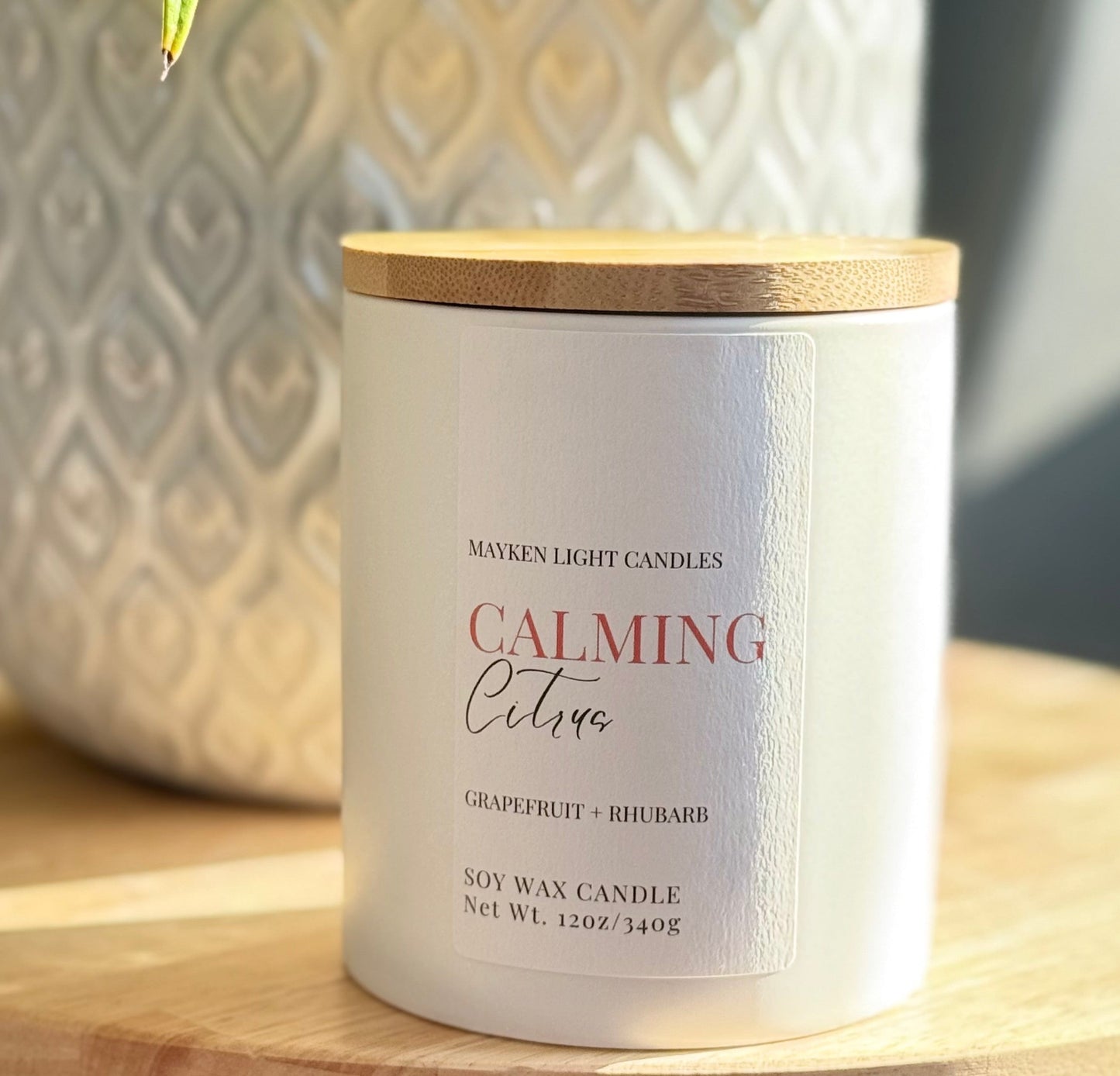 A white candle with a wooden lid, labeled 'Calming Citrus', made by Mayken Light Candles, with text indicating it is a soy wax candle.