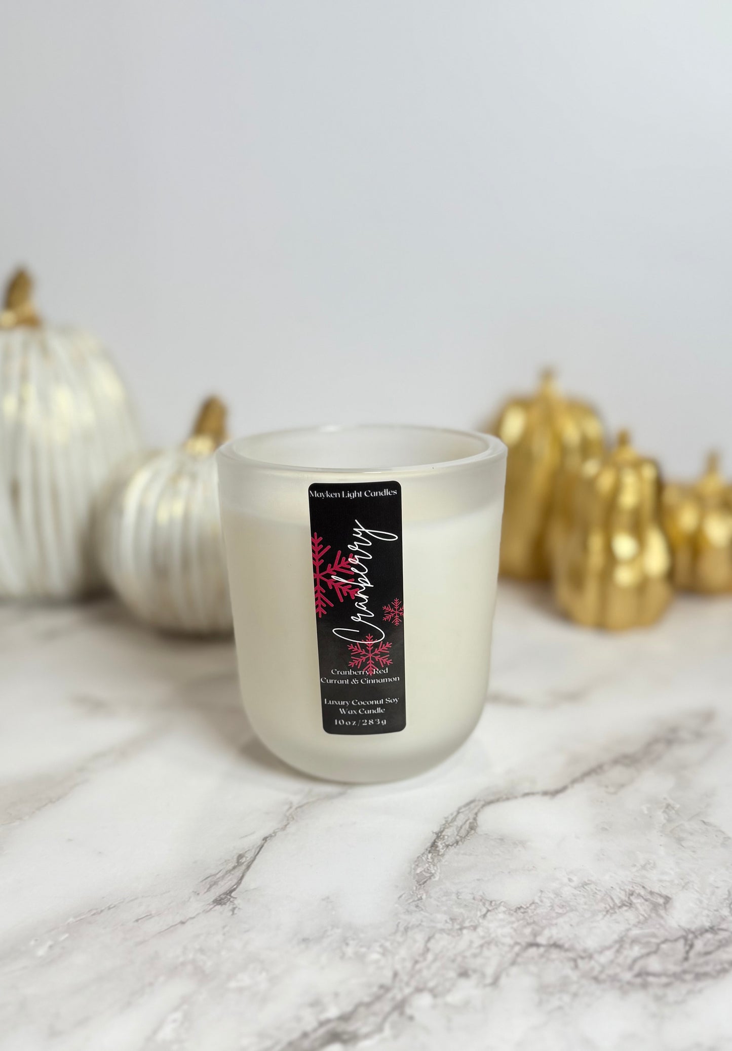 White candle with a label in front of decorative pumpkins on a marble surface