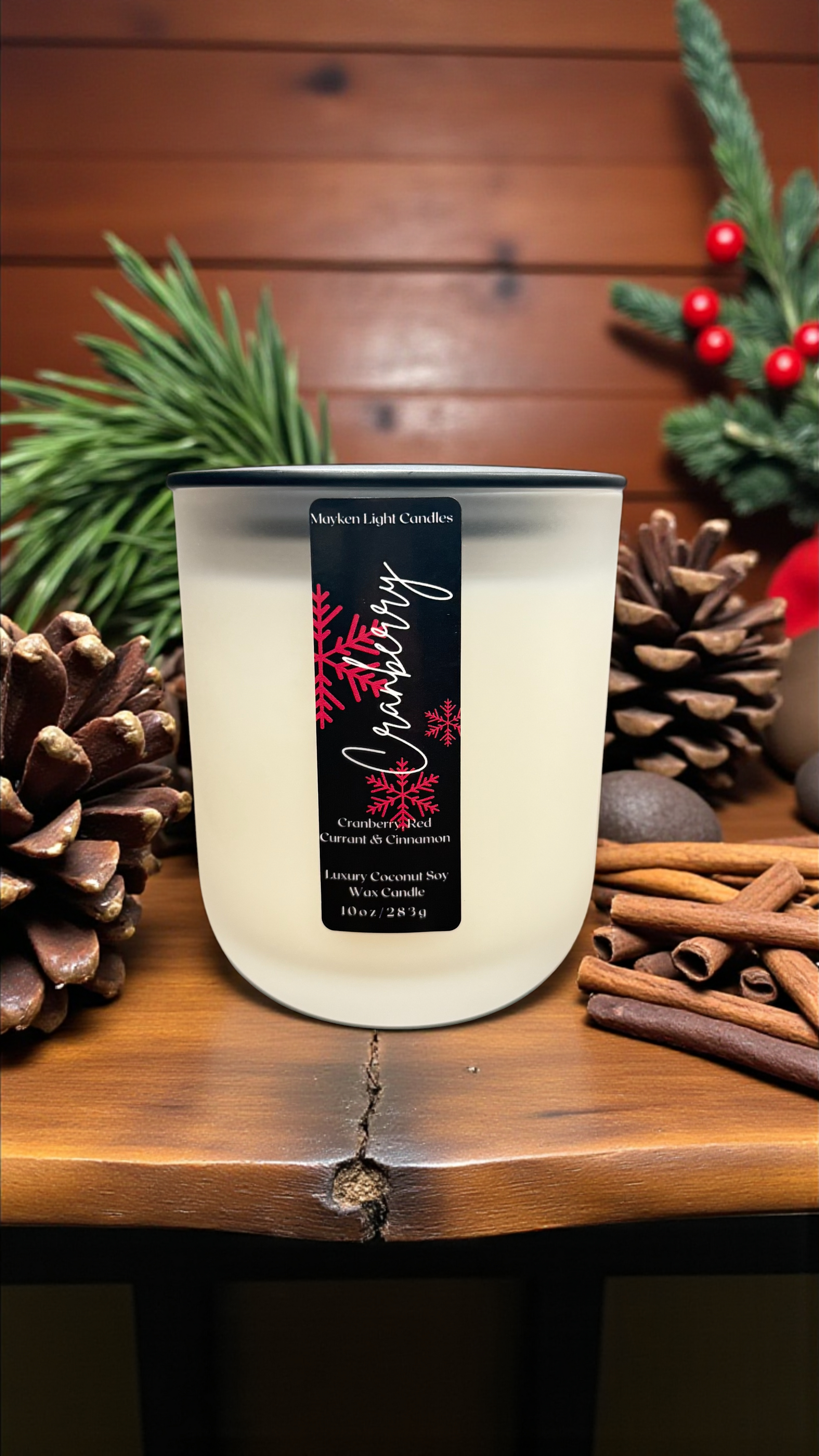 Candle with a decorative label on a wooden surface with pine cones and cinnamon sticks.