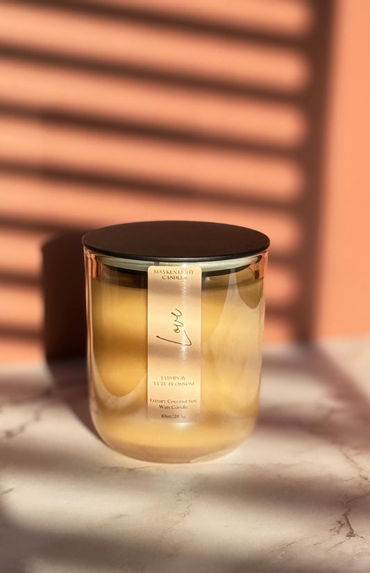 Glass candle with a black lid on a marble surface with a warm light background