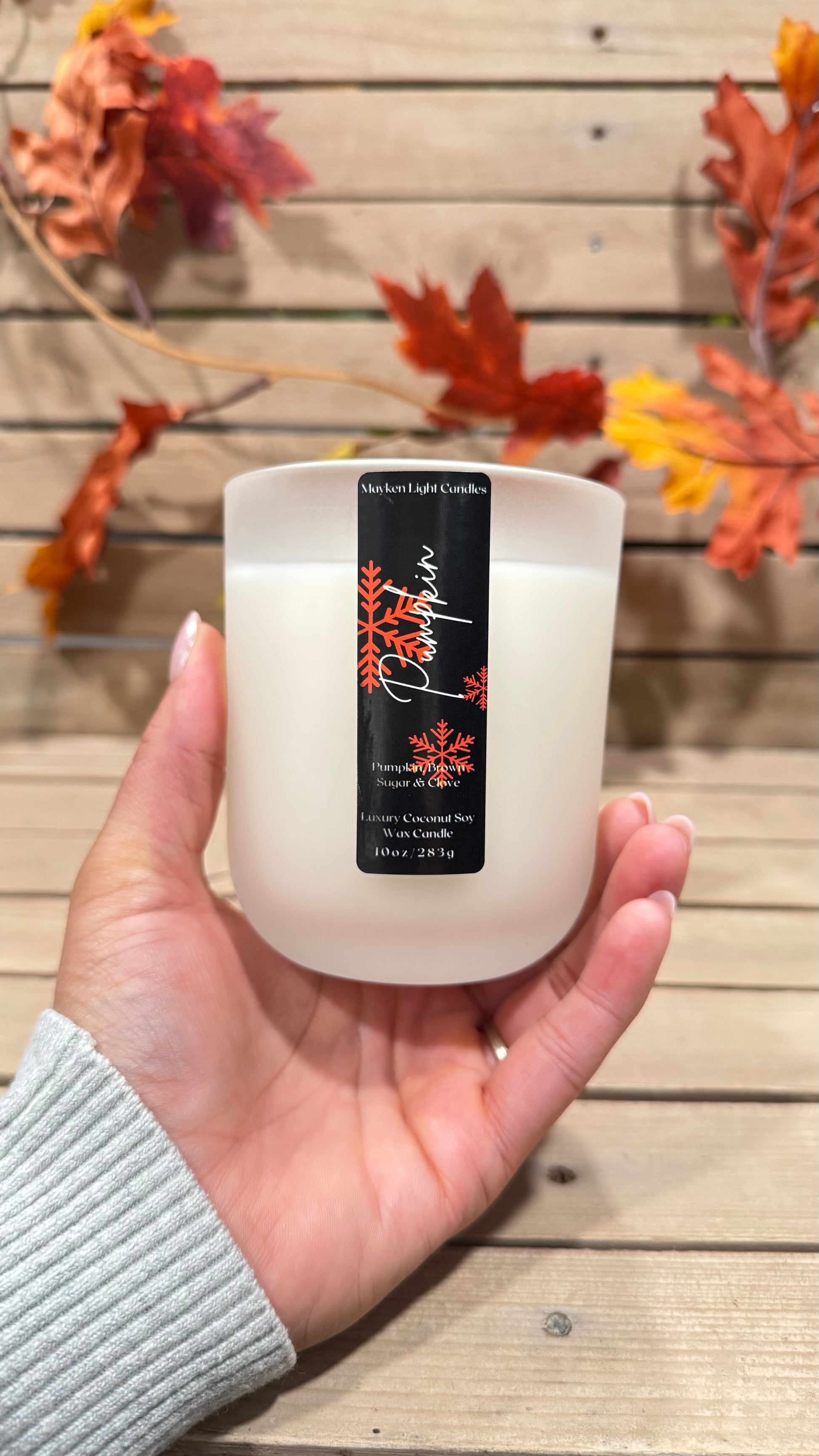 Candle held in a hand with a decorative background of autumn leaves.