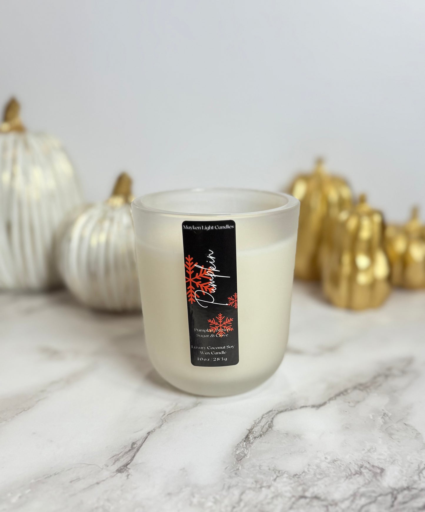 Candle with a label in front of decorative pumpkins on a marble surface
